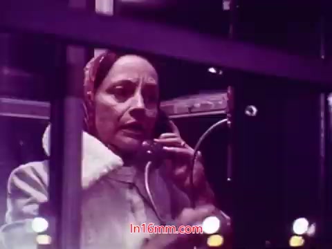 The still from 'Performance' depicts a woman in a coat and a headscarf, speaking into a telephone. She appears focused and serious, conveying a sense of urgency or importance. The background suggests a phone booth setting, with visible equipment, indicating a connection to communication. The film's end titles likely include production details, cast, and crew, providing context to the film's creation in 1971. The overall color tone appears rich and vivid, typical of 16mm prints from that era.