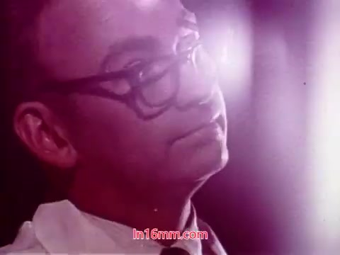 The still from the 16mm film 'Performance' shows a man with glasses, presumably in a professional setting, wearing a white coat and tie. The background appears to have a hazy, illuminated quality, suggesting a focused moment in the film. This image likely represents the tone and subject matter of the film's conclusion, capturing the essence of the narrative and the contributions of the cast and crew during the end titles. The production date signifies its vintage nature, reflecting the stylistic choices of 1971.