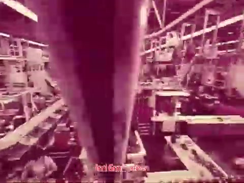 The still from 'Performance' shows an industrial setting, likely a factory or production line, captured in a muted color palette with a pinkish hue. The perspective appears dynamic, possibly from a moving camera or machinery, emphasizing an efficient and busy atmosphere. The image features equipment and workers, hinting at a sense of motion and activity. The end titles are displayed prominently, providing production details and credits.