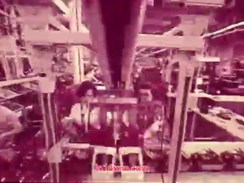 This still from the 1971 film 'Performance' by Bell System depicts a factory setting, showcasing machinery and workers engaged in an industrial process. The image features a perspective that emphasizes both the equipment and the human element, highlighting the interplay between technology and labor. The color palette is likely subdued or monochromatic, typical of the era's film style. This particular frame represents the end titles, providing essential information about the production date and the cast and crew involved.
