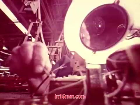 The still from 'Performance' - a Bell System film from 1971 showcases an industrial setting. In the foreground, a hand is seen manipulating equipment, likely related to telecommunications. A bright circular light source adds to the scene's focus, highlighting the details of the machinery. The overall atmosphere reflects the film's exploration of technological processes and human interaction within an industrial context. The still likely serves as an important concluding visual, accompanied by the end titles that detail the production date and credits.