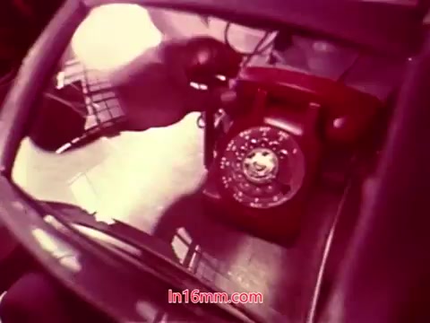 The still from 'Performance' - Bell System Film (1971) features a vintage red rotary telephone resting on a glossy surface. The reflection adds depth, showing a glimpse of the surrounding environment or objects. It's likely part of the film's ending sequence, highlighting its era and aesthetic. The end titles convey production details, including the date and the cast and crew involved. The colors are warm, contributing to the nostalgic feel of the film.