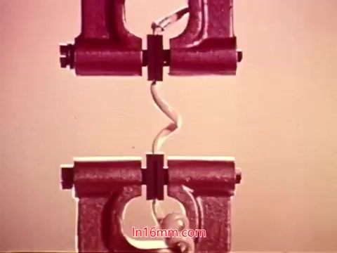 The still from 'Performance' (1971) features a close-up of a mechanism, possibly related to telecommunications, showcasing two metallic parts designed to fit together. A coiled wire connects them, indicative of connections in telephone systems. The background has a soft hue, drawing attention to the mechanical components. This image likely serves as part of the film’s closing sequence, reflecting its technical themes and the collaborative efforts of cast and crew.