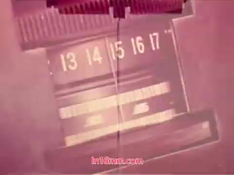 The still shows a close-up of a 16mm film reel, focusing on the filmstrips marked with numbers 13 to 17. The film appears to be in a pinkish hue, suggesting a vintage or altered color presentation typical of older prints. This indicates it's part of the end credits sequence from the 1971 film 'Performance,' highlighting production details like the date and names of the cast and crew involved. The image captures the tactile nature of film projection, showcasing the physical characteristics of film reels.