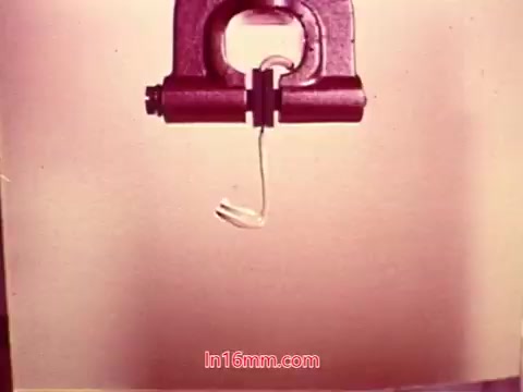 The still from the 16mm film 'Performance' by Bell System from 1971 depicts a close-up view of a mechanical device gripping a thin, flexible piece of material. The background is a muted color, enhancing the focus on the action of the grip. The end titles likely feature production details, including the date and credits for the cast and crew involved in the film. This context suggests a technical or instructional theme characteristic of the era's educational films.