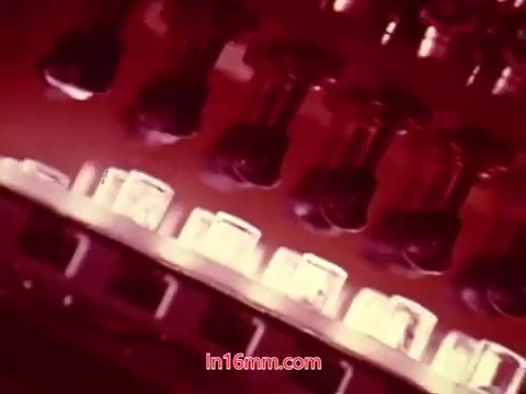 The still from the 16mm film 'Performance' (1971) captures a close-up view of film reels and projectors, showcasing intricate mechanical details. The colors appear rich, possibly with warm tones, emphasizing the vintage aesthetic of the print. This segment likely presents the end titles, which include the production date and credits for the cast and crew involved in the film. The overall texture suggests the film's age, reflecting its 16mm origins.