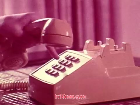 The still from the 16mm film 'Performance' showcases a close-up of a hand reaching for a vintage telephone, immediately setting a nostalgic tone. The telephone is an old model with a rotary dial, suggesting a classic era of communication. The background features soft, muted colors, enhancing the film's vintage aesthetic. This image captures a moment likely related to the film's themes surrounding communication and connection, serving as a fitting visual for the end titles that credit the production date and cast and crew involved.
