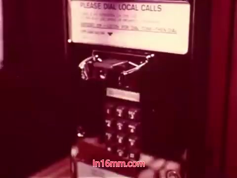 The still from the film 'Performance' shows a vintage payphone, featuring a keypad and a notice indicating to 'PLEASE DIAL LOCAL CALLS.' The lighting suggests a nostalgic, possibly retro atmosphere, characteristic of films from the early 1970s. The scene is likely part of the end titles, featuring production details and credits. This print retains the unique qualities of a 16mm film, hinting at its historical significance within the context of telecommunications of that era.