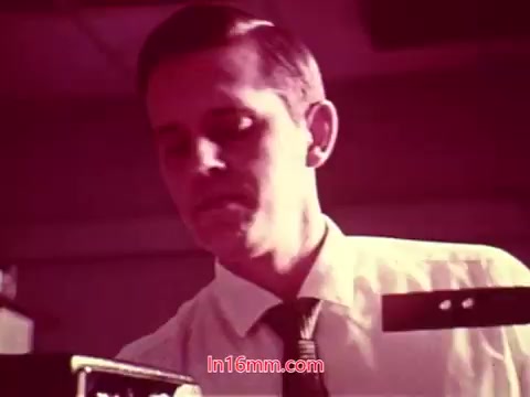 The still from 'Performance' features a man in a light-colored shirt and tie, focused on equipment in an office-like setting. The image has a vintage quality typical of 16mm film, with rich colors and some graininess. The scene likely captures a moment of concentration, possibly related to the film's themes. The end titles, which you note are present, provide production details, including the date and contributions of the cast and crew.