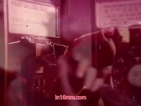 The 16mm still from 'Performance' (1971) features a close-up of a payphone, emphasizing the tactile interaction of a hand manipulating the phone. The scene is imbued with a warm, reddish hue, creating a retro aesthetic typical of the film's era. This particular frame includes end titles that provide details about the production date and credits for the cast and crew, encapsulating the film's narrative closure.