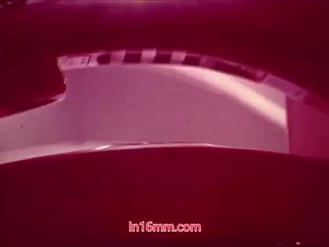 The still from the 16mm print of 'Performance' (1971) captures a close-up view of a curved surface, possibly a part of the film's set or a prop. The image is characterized by a reddish hue, indicative of the film's color grading. The composition emphasizes smooth lines and shapes, a stylistic choice that serves to create a visually striking effect. This segment likely corresponds to the film's end titles, providing credits for the cast and crew, and marking the film's conclusion.