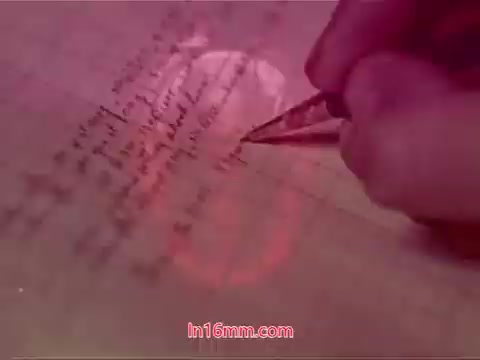 The still from 'Performance' depicts a close-up of a hand writing with a pen on lined paper. The shot is captured in a warm color tone, adding a nostalgic feel. The background has a slight blur, drawing attention to the writing process. This frames the end titles, which likely include the production date and credits for the cast and crew. The image embodies a reflective moment, encapsulating the conclusion of the film.