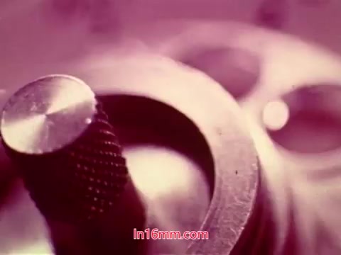 The still features a close-up of a part of a film projector, likely capturing a metallic component with intricate details. The image has a soft, warm tint, suggesting a vintage quality typical of 16mm prints. The context of this shot indicates it is part of the end titles from 'Performance,' showcasing production details. The focus on machinery emphasizes the film's technical aspects, aligning with its thematic exploration of performance and representation.