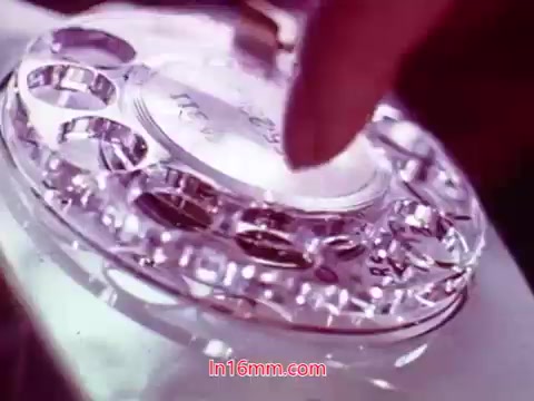 The still from the film 'Performance' features a close-up of a vintage rotary phone, with a hand poised to dial. The background showcases a soft blur, emphasizing the phone's intricate design and craftsmanship. The image captures a moment of interaction with technology, evoking nostalgia for the era. The film's end titles are present, detailing production dates and credits for the cast and crew.