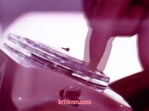 The still from 'Performance,' a Bell System film from 1971, showcases a close-up of a hand interacting with a transparent disc or dial. The colors appear soft and slightly faded, typical of 16mm prints. The focus on the hand suggests a moment of action or adjustment, capturing the tactile nature of the film’s subject matter. This frame contributes to the overall aesthetic and thematic elements of the film, which includes end titles detailing production information and credits.