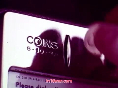 The 16mm still from 'Performance' features a close-up of a coin slot on a payphone, with a hand inserting a coin. The focus is on the metallic surface, showcasing the details such as the word 'COINS' and the slot labeled for coin insertion. The aesthetic likely reflects the film's era in 1971, with a muted color palette typical of that time. This still may serve as an evocative moment within the film, highlighting themes of communication or connection.