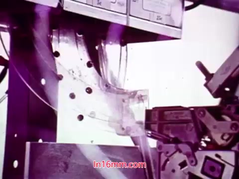 The still from the 16mm film 'Performance' - Bell System Film from 1971 likely features a close-up of a film projection or processing equipment. The focus is on mechanical elements, showcasing components like film reels, splices, or a film feed mechanism. The colors may appear slightly altered, possibly with a purple hue, reflecting the film's vintage quality. This frame captures a moment of technology in action, indicative of the era's filmmaking processes.