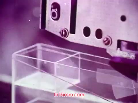 The still appears to depict a close-up of a mechanical device working with a transparent object, possibly made of plastic or glass. The machine, likely part of the production process, is shown in a detailed manner, with vibrant colors and a slightly abstract aesthetic. The context suggests it is from the end titles of the film, which include production details and credits. The focus on both the technology and the object hints at themes of innovation or industry central to the film's narrative. The overall mood is technical and visually engaging, reflecting the film's production era.