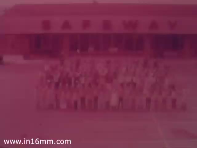 The still features a large group of people gathered in front of a Safeway grocery store, showcasing a community or staff event. The building prominently displays the Safeway logo. The image has a vintage aesthetic typical of 1970s commercial promotional materials, with muted colors and a nostalgic feel.