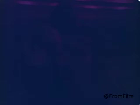 The still features the Kool-Aid Man, an iconic, anthropomorphic pitcher filled with cherry Kool-Aid, bursting through a wall or backdrop filled with vibrant colors typical of the 1970s. His cheerful demeanor and playful nature are central to the scene, reflecting the character's role in advertising as a fun-loving figure who answers the call of children for refreshment. The image captures the whimsical essence of the era's commercials.