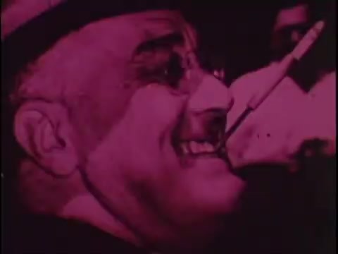 The still from the 1977 Sikorsky S-76 promo film features a close-up of a smiling man, likely conveying a sense of joy or enthusiasm. The image has a distinct pop art aesthetic, characterized by a bold pink hue. The man's glasses and hat add to the vintage feel, suggesting a connection to the historical context of the era. The overall composition hints at a celebratory or noteworthy moment, aligning with the film's intention to showcase the Sikorsky S-76 in a compelling way.