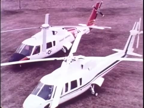 The still from the 1977 Sikorsky S-76 promo film features two Sikorsky S-76 helicopters positioned on a grassy landscape. One helicopter is painted in a white and black scheme, while the other has a distinctive red and white livery, suggesting a connection to the Coast Guard. The shot captures the sleek design and rotor blades of the helicopters, illustrating their modern engineering. The absence of sound leaves the viewer focused on the visuals, highlighting the helicopters' features and capabilities in a silent yet impactful presentation.