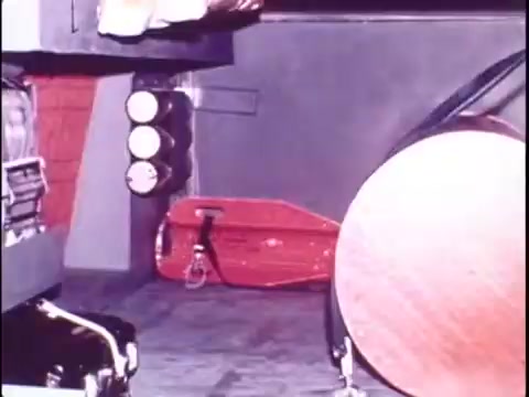 The still from the Sikorsky S-76 promo film features a close-up shot of aircraft components. The scene includes visible elements such as metallic panels and possibly part of the cockpit, with a bright red object suggesting safety equipment or a tool. The lighting suggests a technical environment, emphasizing the engineering and design aspects of the Sikorsky S-76. The focus on details highlights the craftsmanship involved in the helicopter's construction, all while maintaining a silent, workprint quality indicative of the era.