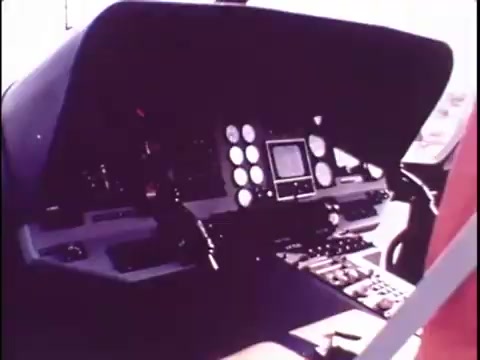 The still showcases the cockpit of the Sikorsky S-76 helicopter, emphasizing the control panel filled with a variety of dials, switches, and displays. The design appears modern for its time, highlighted by a clean layout that suggests advanced technology. The absence of sound from the promo film leaves the visual elements to convey the sophistication and innovation of the S-76, which was likely intended to appeal to potential clients. The overall aesthetic reflects the era's graphic style, transitioning from the earlier pop art visuals of presidents to this technical focus on aviation.