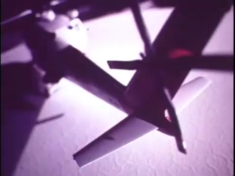 The still features a close-up view of the Sikorsky S-76 helicopter model, showcasing its sleek design and structural details. The lighting creates dramatic shadows, emphasizing the contours of the aircraft. The background appears blurred, likely to focus attention on the model. This image encapsulates the promotional essence of the film, highlighting the innovative design of the S-76 amidst a creative visual style.