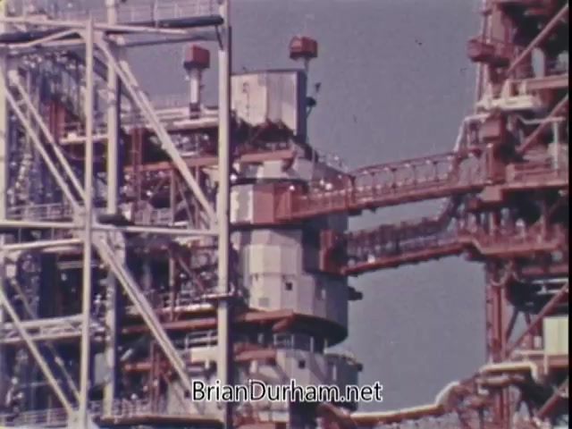 The still features a structured industrial scene, likely from a NASA facility. It showcases a complex arrangement of metallic frameworks and machinery, highlighting the intricacies of space technology. This visual underscores the theme of aspiration and achievement, as Jim Lovell, an astronaut, emphasizes that anyone, especially youth, can reach impressive heights through physical fitness and dedication. The imagery connects with Lovell's message of limitless possibilities.