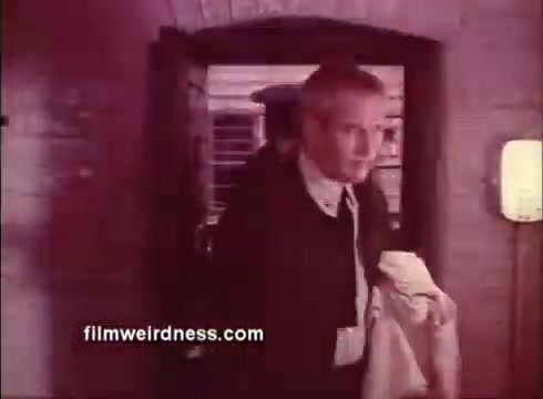 The still from the trailer of 'The Mackintosh Man' features a scene with a character, portrayed by Paul Newman, stepping through a doorway. He appears to be engaged in a tense moment, suggesting themes of intrigue or espionage. The vintage aesthetic of the 16mm film adds a nostalgic quality to the image. The atmosphere hints at a dramatic narrative typical of the thriller genre.