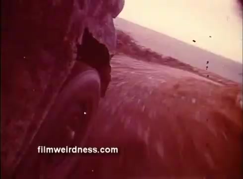 The still from 'The Mackintosh Man' trailer captures a low-angle shot of a vehicle's wheel in motion, kicking up dirt and debris. The blurred background suggests speed and urgency, hinting at a tense, action-filled scene. The color palette appears warm and slightly faded, characteristic of vintage film.