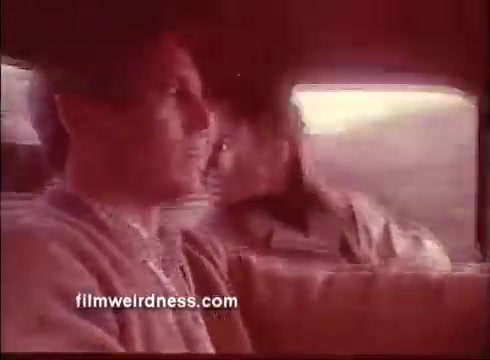 The still from the trailer of *The Mackintosh Man* features Paul Newman in profile, sitting in the backseat of a car. The interior has a warm, muted color palette. Another character is visible in the background, glancing out the window. This moment likely captures a tense or contemplative atmosphere, hinting at the film's themes of intrigue and suspense.