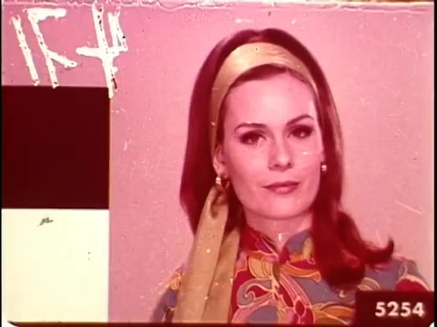 The still from '16mm leader China Girls' features a woman with a stylish appearance, donning a colorful patterned top and a matching headband. The image is likely intended for color testing in film processing, showcasing vibrant hues alongside color bars for reference. Overall, it captures a retro aesthetic typical of the film era.