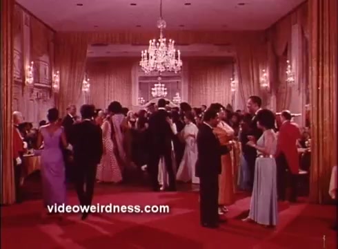 The still features a lively scene from a ballroom, depicting a crowd of elegantly dressed individuals dancing and socializing. The room is adorned with luxurious chandeliers and rich drapery, creating a glamorous atmosphere typical of the Blaxploitation genre. The vibrant colors and diverse outfits hint at a celebratory occasion, embodying the film's spirited tone. Overall, it captures the essence of social gatherings in the 1970s.