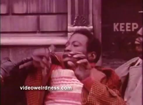 The still from 'Come Back, Charleston Blue' features a scene characteristic of the Blaxploitation genre. It captures a moment with a man in a vibrant, patterned outfit, appearing animated in his expression. The background suggests an urban setting, hinting at themes of community and street life. The overall aesthetic reflects the bold colors and stylized visuals typical of the film's era.