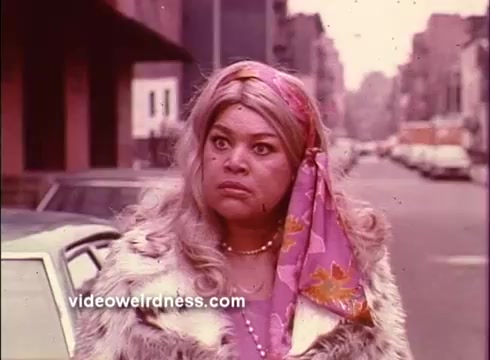 The still from 'Come Back, Charleston Blue' features a woman with striking features, wearing a glamorous outfit with a fur coat and a colorful scarf. She looks serious or concerned, set against an urban street backdrop. The color palette suggests a vintage feel, typical of the blaxploitation genre.