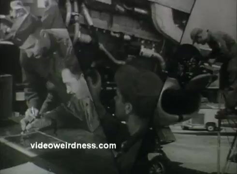 The still from 'Russ Hodges Air Force PSA - 1950s' features a montage of Air Force personnel engaged in various activities. One soldier is seen writing or drawing on a large surface, while others focus on technical equipment and machinery. The overall tone suggests a behind-the-scenes look at Air Force operations, highlighting teamwork and technical skills. The image likely aims to promote pride and awareness of the Air Force's role in the 1950s.
