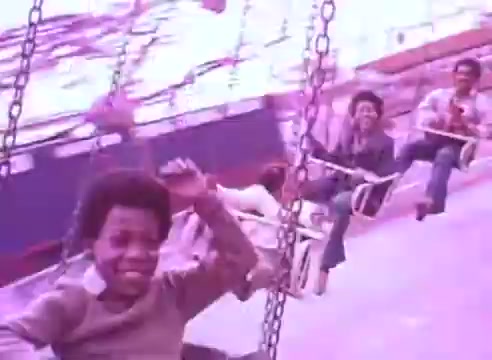 The still shows a nostalgic scene of children enjoying a fairground ride, likely a swing carousel. The atmosphere is joyful, with kids smiling and laughing, emphasizing carefree moments. The color palette has a slightly faded, retro quality, hinting at a vintage aesthetic. The context suggests a connection between maintaining health, such as taking blood pressure medication, and enjoying life with loved ones.