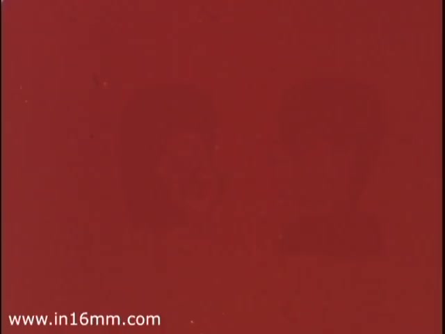 The still from the 'Florient Air Freshener' commercial features a background of deep red, with two indistinct figures appearing faintly. This aesthetic aligns with the vibrant and bold advertising trends of the 1970s, often characterized by striking colors and an emphasis on sensory appeal, particularly in fragrance-related products. The quality of the image suggests it's a 16mm print, typical of the era for commercials.