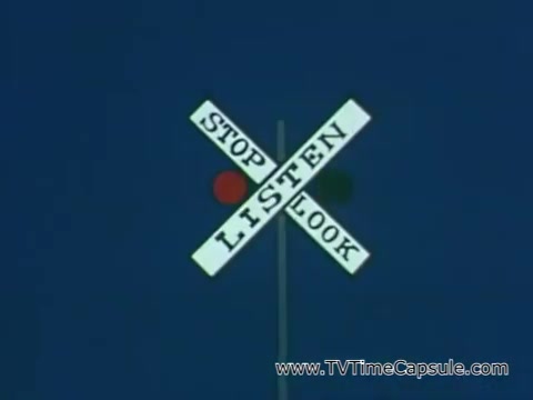 The still features a railroad crossing sign with three key safety instructions: 'STOP,' 'LISTEN,' and 'LOOK.' It is presented against a blue background, emphasizing the importance of vigilance in safety. This visual aligns with the message from the context about being attentive to safety signals, particularly regarding pesticide usage and labels.