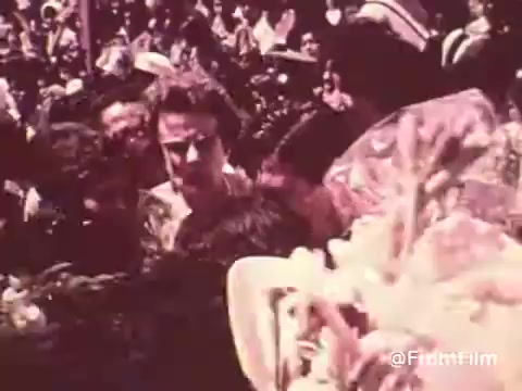 The still from the 'Project Hope Public Service Announcement - 60's/70's' likely captures a crowded scene, reflecting the humanitarian efforts of Project HOPE. It features a diverse group of people, perhaps during an event or gathering, conveying a sense of community and collaboration. The vibrant colors typical of that era enhance the emotional impact, underscoring the organization's mission to provide health care and assistance globally. The atmosphere suggests urgency and dedication to improving health opportunities.