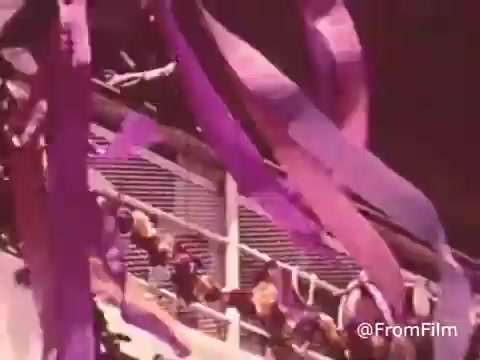 The still captures a vibrant scene with colorful purple ribbons cascading down from a structure, likely representing celebration or hope. This imagery is tied to the ethos of Project HOPE, emphasizing health and humanitarian efforts. The overall atmosphere suggests a sense of community support and optimism associated with the organization's mission during the 1960s and 70s.