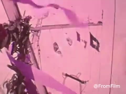 The still from 'Project Hope Public Service Announcement - 60's/70's' features a vibrant display likely from a ship, with colorful ribbons and flags adorning the masts. The scene is tinted with a pink hue, adding a nostalgic and hopeful atmosphere. This imagery reflects the spirit of Project HOPE, emphasizing health and wellness initiatives during that era, particularly through the work of the SS HOPE hospital ship.