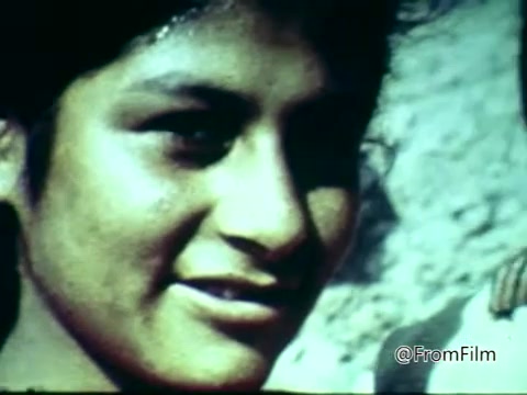The still shows a close-up of a young person with a slight smile, highlighting their expressive features. The image appears to be taken outdoors, with a textured background that suggests a natural setting. The color tones indicate an older film quality, typical of 16mm cinematography from the 1970s. This frame likely captures a moment intended to convey warmth and connection, characteristic of public service announcements aimed at raising awareness.