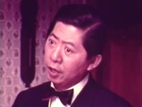 The still from the 1973 Chun King Chinese Food commercial features an expressive male character, likely Charles Louie, dressed in a tuxedo. His animated facial expression suggests he is conveying excitement or enthusiasm, fitting for a festive and engaging advertisement. The background, with patterned wallpaper, hints at a homey setting, appropriate for a family-oriented commercial. This nostalgic piece captures a moment in advertising history and reflects the cultural touchpoints of its time, making it a meaningful Christmas gift.