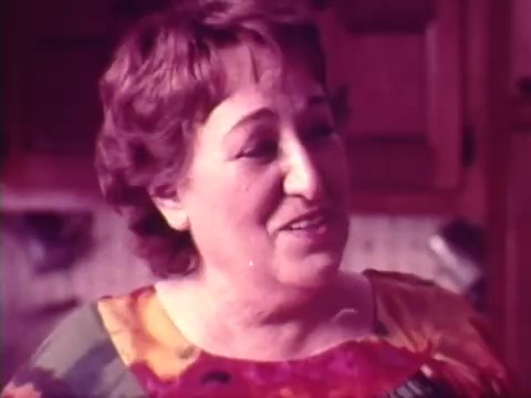 The still from the 'Chun King Chinese Food Commercial with Mama Cass' features a woman who exudes warmth and personality, likely portraying a comforting maternal figure. She is dressed in a colorful, floral-patterned shirt, which adds vibrancy to the scene. The setting appears to be a cozy kitchen, hinting at a familial and inviting atmosphere. This commercial, dating back to 1973, captures a nostalgic moment connected to both food and family, making it a meaningful gift.