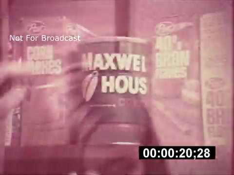 The still from the 1968 Maxwell House Coffee commercial titled 'The Father's Story' features a close-up of a can of Maxwell House coffee amidst a backdrop of cereal boxes. The overall aesthetic has a vintage look with a slightly muted color palette, emphasizing a nostalgic feel. The scene likely conveys themes of family and togetherness, typical of advertisements from that era, and the visual context suggests a focus on coffee as a staple for family moments. The mention of '#cringeworthy' hints at its datedness and possibly over-the-top sentimentality characteristic of commercials from that time.