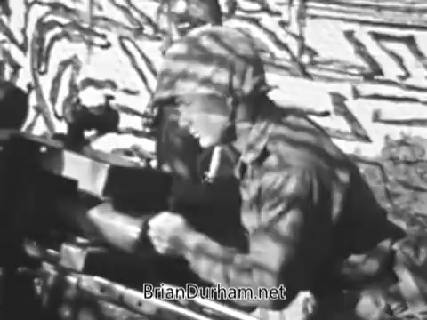 The still shows a U.S. Marine in uniform, focused on operating a weapon, likely during a training or combat scenario. The environment features camouflage and military gear, emphasizing the intensity of Marine duties. The context suggests various roles available in the Marines, from aircraft mechanics to combat positions, highlighting the diverse experiences servicemen might encounter.