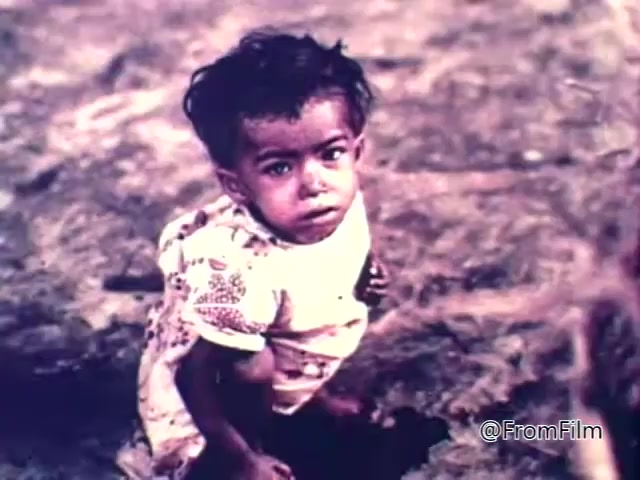 The still from the 1975 CARE World Hunger Fund PSA features a young child sitting on the ground, looking directly at the camera. The child has unkempt hair and is wearing a simple, patterned shirt. The background appears dry and desolate, emphasizing the theme of hunger and hardship associated with the campaign. The image conveys a poignant sense of vulnerability, aiming to raise awareness about global hunger issues.